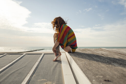 Woman with tattoo crouching on plank, looking at the sea - KNSF04343