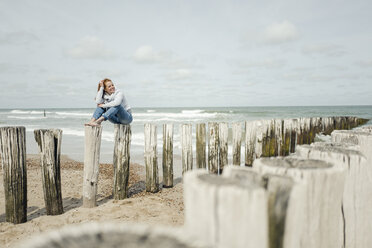 Frau sitzt auf einem Zaun am Strand und entspannt sich am Meer - KNSF04344