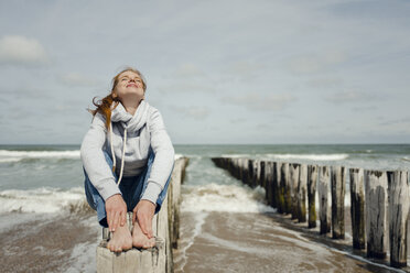 Frau sitzt auf einem Zaun am Strand und entspannt sich am Meer - KNSF04345