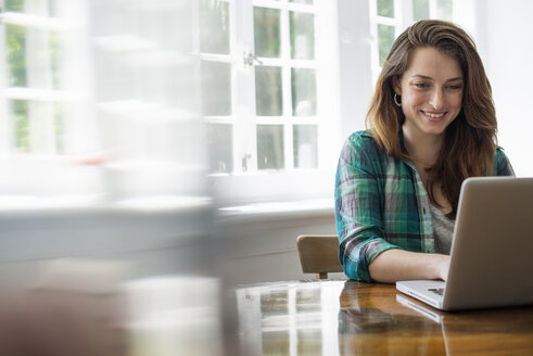 Smiling woman with laptop in home office. - MINF01732