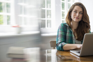 Smiling woman with laptop in home office. - MINF01733