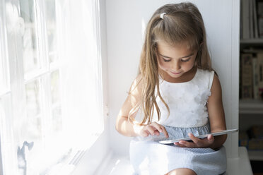 Ein junges Mädchen sitzt auf einem Fensterplatz und benutzt ein digitales Tablet. - MINF01769