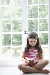 Ein Mädchen sitzt beim Spielen und hält ein Smartphone in der Hand. - MINF01771