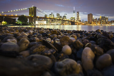 Nächtlicher Blick auf Manhattan von Brooklyn aus, mit der Brooklyn Bridge, die den East River überspannt, und dem felsigen Ufer im Vordergund. - MINF01781