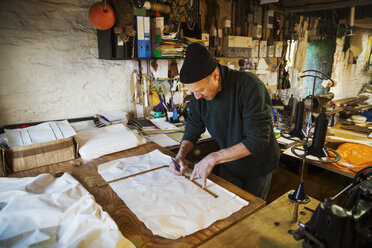 Man in a sailmaker's workshop measuring a piece of fabric for a sail. - MINF01797