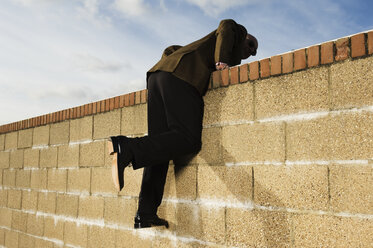 Side view of man wearing a suit climbing over yellow brick wall. - MINF01800