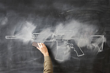 Person löscht Kreidezeichnung einer Pistole auf einer Tafel - ISF16985