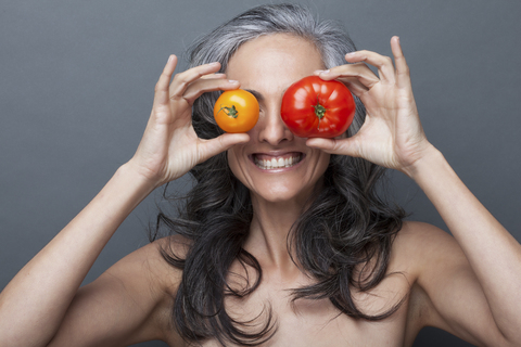 Reife Frau bedeckt Augen mit roter und gelber Tomate, lizenzfreies Stockfoto
