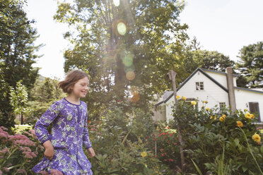 Ein Kind in einem gemusterten blauen Kleid läuft durch einen Hausgarten. - MINF01832