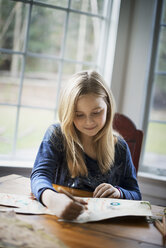 Ein Familienhaus. Ein junges Mädchen sitzt an einem Tisch und zeichnet auf einem großen Blatt Papier. Sie hält einen Bleistift. - MINF01837
