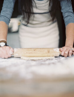 Eine häusliche Küche. Eine Frau bereitet eine Mahlzeit vor. Sie rollt Gebäck auf einer Tischplatte aus. - MINF01854