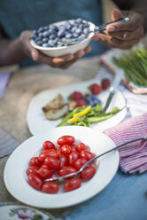 Ein Familienpicknick im Schatten hoher Bäume: Eltern und Kinder bedienen sich an frischem Obst und Gemüse. - MINF01864