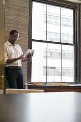 Ein Mann steht an einem Fenster in einem Büro und benutzt ein digitales Tablet. - MINF01893