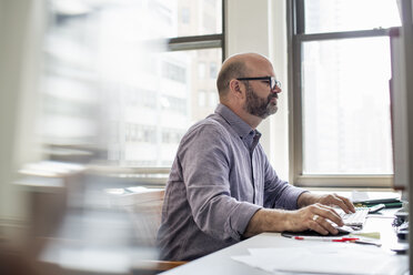 Büroalltag: Ein Mann sitzt an einem Schreibtisch mit einem Computer und blickt konzentriert auf den Bildschirm. - MINF01909