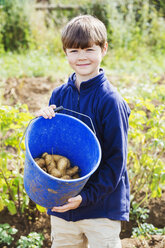 Ein Junge hält einen Eimer mit Kartoffeln auf einem Feld. - MINF01928
