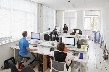 A modern office, workstations for staff. Elevated view of six people seated at desks. A man using an ergonomic kneeler chair. - MINF01948