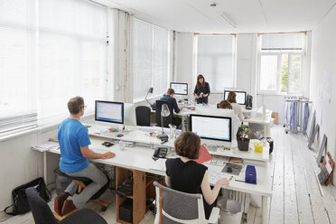 Ein modernes Büro mit Arbeitsplätzen für Mitarbeiter, sechs Personen an Schreibtischen, ein Mann auf einem ergonomischen Kniestuhl. - MINF01948