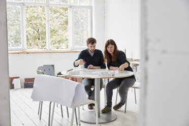 Ein modernes Büro, zwei Personen bei einer Besprechung, die Pläne besprechen, Architekturzeichnungen und Gebäudemodelle. - MINF01950