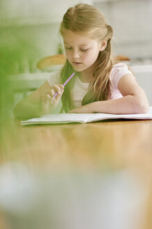 A girl seated at a table with a pencil, doing her homework. - MINF01965