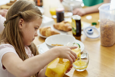 Eine Familie beim Frühstück, ein Mädchen gießt Orangensaft in ein Glas. - MINF01969