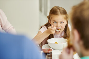 Eine Familie frühstückt, ein Mädchen isst Müsli mit einem Löffel. - MINF01971
