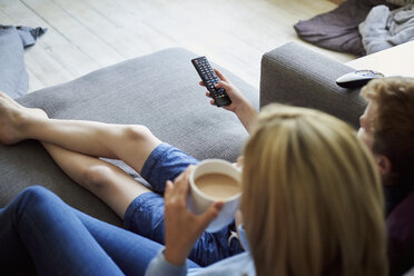 A woman sitting with a cup of tea holding the television remote control in her hand. - MINF01975