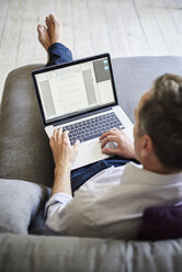 Ein Mann, der auf einem Sofa sitzt und einen Laptop benutzt, Blick über die Schulter. - MINF01979