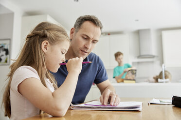 A young girl and her father sitting looking at her school books, doing her homework. - MINF01983