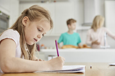 Ein Mädchen sitzt am Tisch in der Küche der Familie, hält einen Bleistift in der Hand und macht Hausaufgaben. - MINF01984