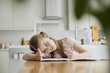 Ein Mädchen, das am Tisch in der Küche der Familie sitzt, einen Bleistift in der Hand hält und den Kopf in die Hände stützt. - MINF01985