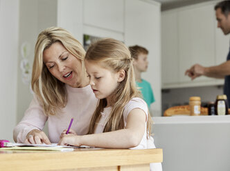 Eine Frau und ihre Tochter sitzen an einem Tisch in der Küche und sehen sich ihre Hausaufgaben an. - MINF01986