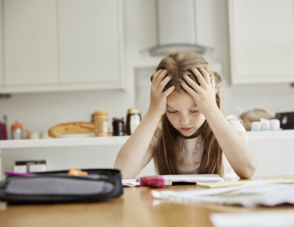 A girl sitting at a table with her hands on her head, looking at her homework. - MINF01987