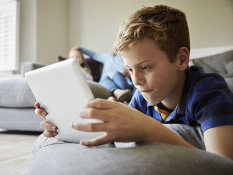 Ein Junge liegt auf dem Boden und schaut auf ein digitales Tablet. - MINF01999