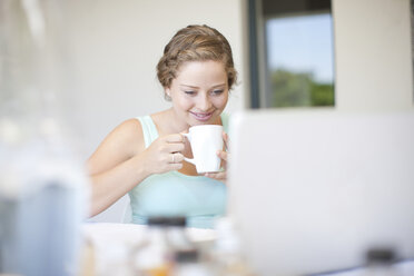 Junge Frau, die einen Laptop benutzt und Tee trinkt - ISF17005