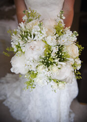 Eine Frau in einem weißen Kleid, eine Braut mit einem Brautstrauß aus weißen Blumen, großen weißen Rosen und Pfingstrosen, mit zarten gelben Blüten und grünen Blättern. - MINF02107