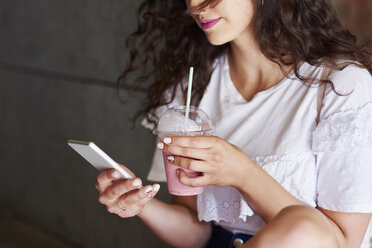 Eine Frau hält ihr Smartphone und eine Tasse Smoothie in den Händen - ABIF00745