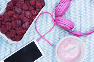 Box of raspberries, smoothie, smartphone and pink headphones on blanket - ABIF00747