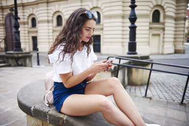 Junge Frau sitzt auf einer Mauer und benutzt ein Mobiltelefon - ABIF00754