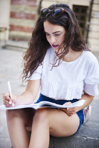 Porträt einer jungen Frau, die im Freien sitzt und in ein Notizbuch schreibt, lizenzfreies Stockfoto