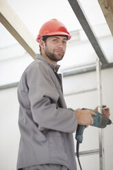 Male laborer on ladders with electric drill on construction site - ISF17069