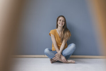 Fröhliche Frau, barfuß und mit gekreuzten Beinen auf dem Boden sitzend, lachend - JOSF02294