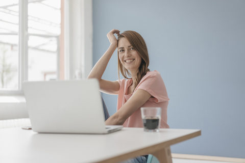 Frau zu Hause sitzt am Schreibtisch mit Laptop, lizenzfreies Stockfoto