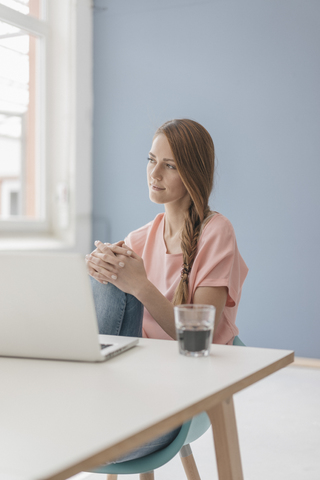 Frau zu Hause sitzt am Schreibtisch mit Laptop, lizenzfreies Stockfoto