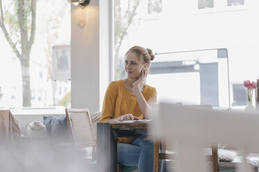 Junge Frau sitzt im Coworking Space und liest Zeitung - JOSF02317