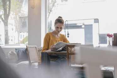 Young woman sitting in coworking space, reading newspaper - JOSF02318