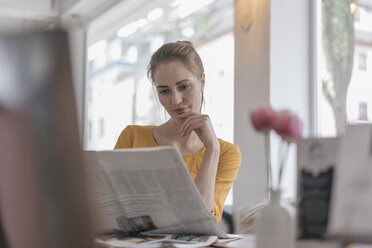 Young woman sitting in coworking space, reading newspaper - JOSF02319