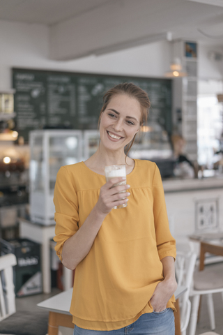 Junge Unternehmerin steht in ihrem Café und trinkt Kaffee, lizenzfreies Stockfoto
