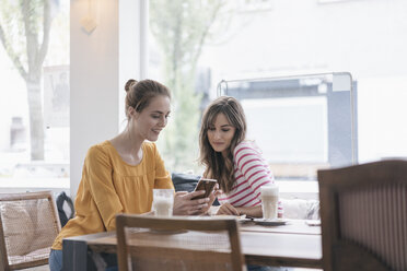 Two girlfriends meeting in a coffee shop, using smartphone - JOSF02335