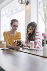 Two girlfriends meeting in a coffee shop, using smartphone - JOSF02337