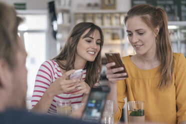 Two girlfriends meeting in a coffee shop, using smartphones - JOSF02342
